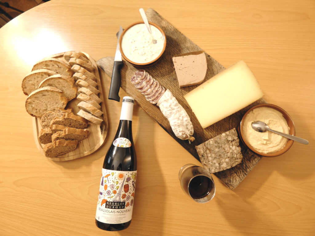 Iconic Beaujolais Nouveau from Georges DuBoeuf paired with a charcuterie board and bread on a plate.