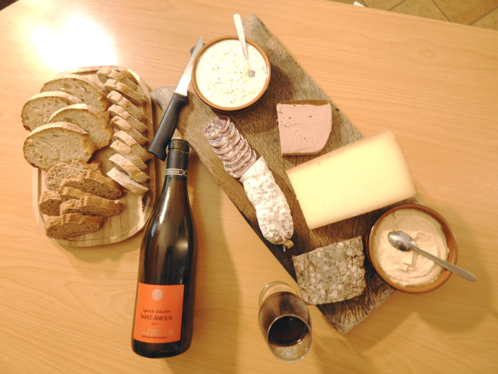 On top view of a charcuterie board and a Saint Amour Beaujolais wine. A sliced bread plate and a glass of wine.