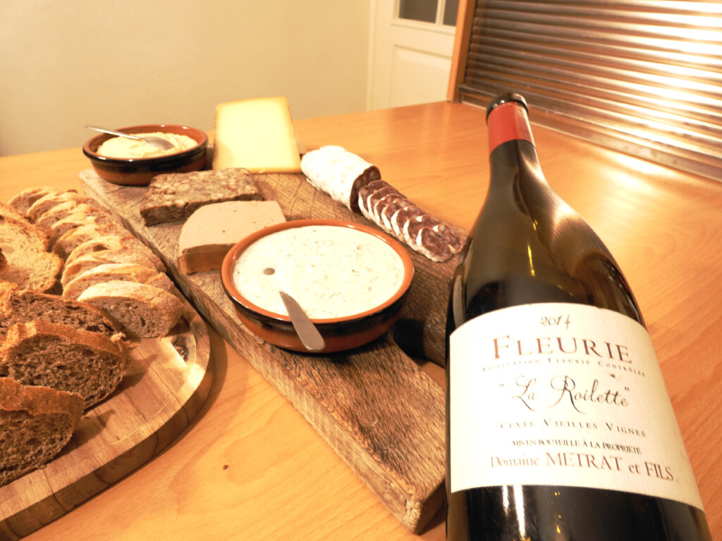 A Fleurie La Roilette bottle of wine from Beaujolais region and a charcuterie board as a matching food.