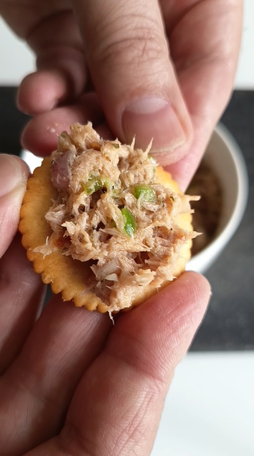 Close-up of tuna rillette spread on a Ritz cracker topped with sun-dried tomatoes, capers, sweet pepper, shallots, ginger, oregano and honey appetizer