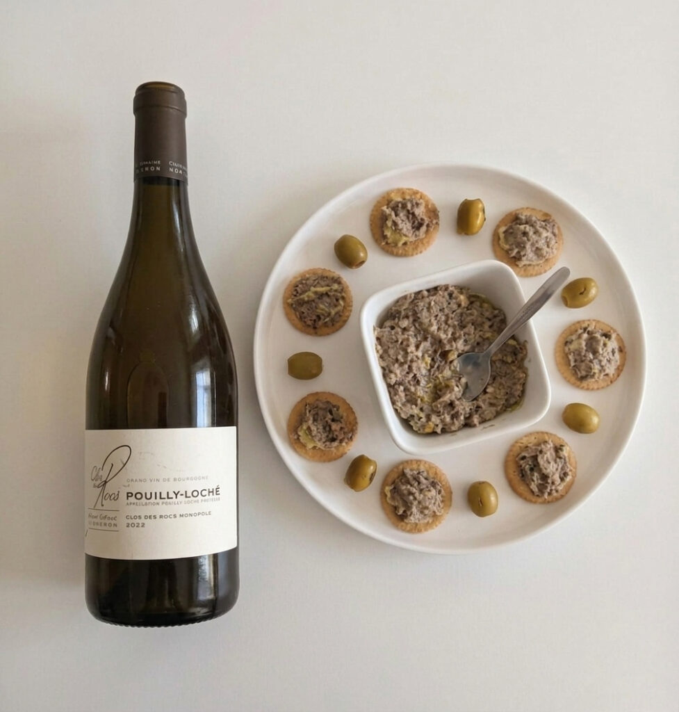 Overhead view of Clos des Rocs Pouilly-Loché wine bottle next to a platter of sardine and avocado spread appetizers on Ritz crackers.