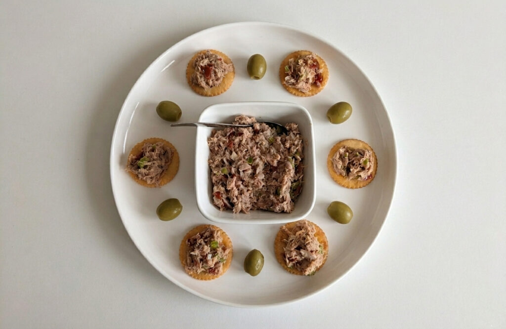 Easy gourmet aperitif ideas with fish spread. Tuna Rillettes taken from the top. Plate with crackers and green olives.