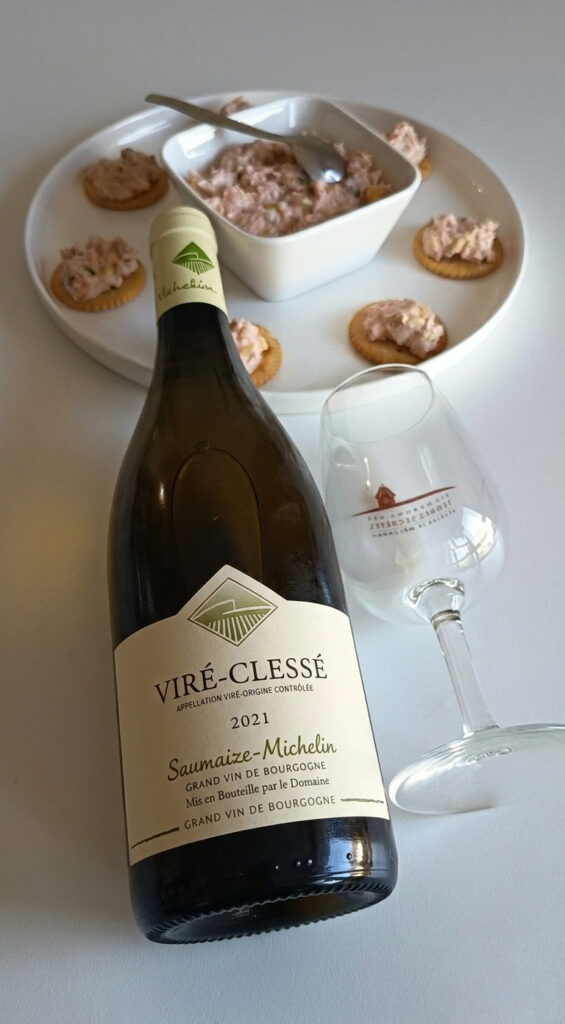 Top-down view of sardine rillette appetizer bites with green olives, capers, sweet pepper, and spring onions paired with a Viré-Clessé white wine from Domaine Saumaize-Michelin, featuring the wine bottle and a wine glass on a rustic table.