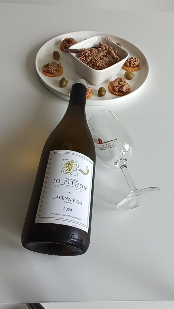 Top-down view of tuna rillette appetizer bites with sun-dried tomatoes and bell pepper paired with a Loire Valley Savennières white wine from Domaine Jo Pithon, featuring the wine bottle and an empty wine glass on a rustic table.