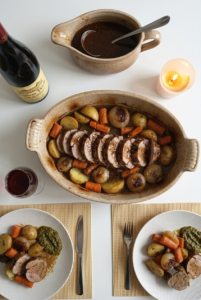 Overhead view of sliced roasted pork tenderloin with potatoes and carrots in a ceramic dish, paired with a bottle and glass of Château Thivin Côte de Brouilly red wine.
